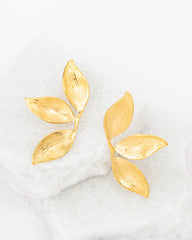 Gold leaf-shaped earrings on a white marble surface