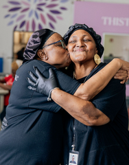 Two women embracing each other in a warm hug with a colorful abstract design in the background.