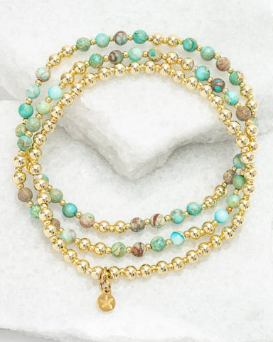 Stack of gold and turquoise beaded bracelets on a white surface