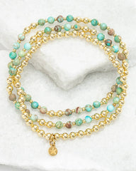 Stack of gold and turquoise beaded bracelets on a white surface