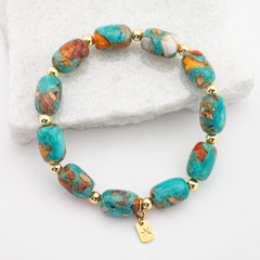Turquoise and gold beaded bracelet on a white stone background