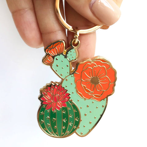 Cactus-shaped enamel keychain in a Paper Anchor Co. packaging on a green marble surface.