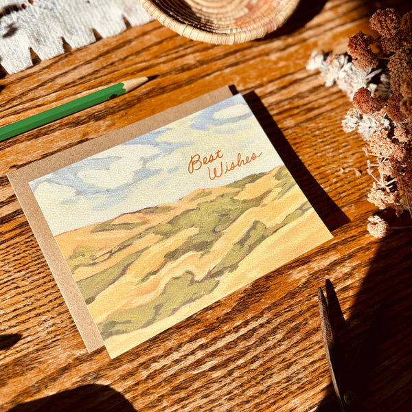 Greeting card with landscape design and 'Best Wishes' text on a wooden surface.